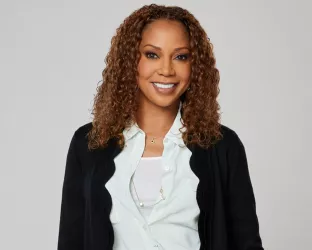Actress Holly Robinson Peete wearing blue trousers and a white button up with a long black cardigan