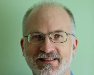An older white man with glasses and a gray beard wearing a blue button up shirt